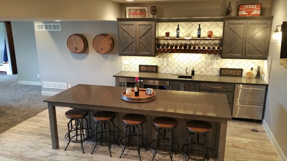 Photo of a large country single-wall seated home bar in Kansas City with an undermount sink, shaker cabinets, dark wood cabinets, solid surface benchtops, white splashback, subway tile splashback, vinyl floors, brown floor and brown benchtop.