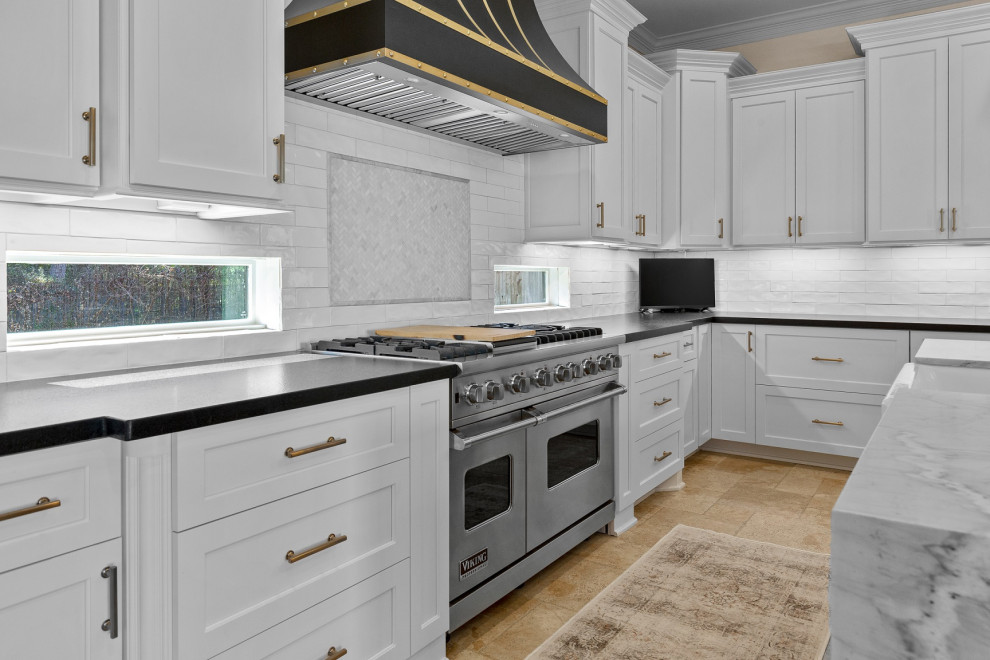 Inspiration for a large transitional l-shaped limestone floor and beige floor eat-in kitchen remodel in Houston with a farmhouse sink, recessed-panel cabinets, white cabinets, quartzite countertops, white backsplash, limestone backsplash, stainless steel appliances, an island and white countertops