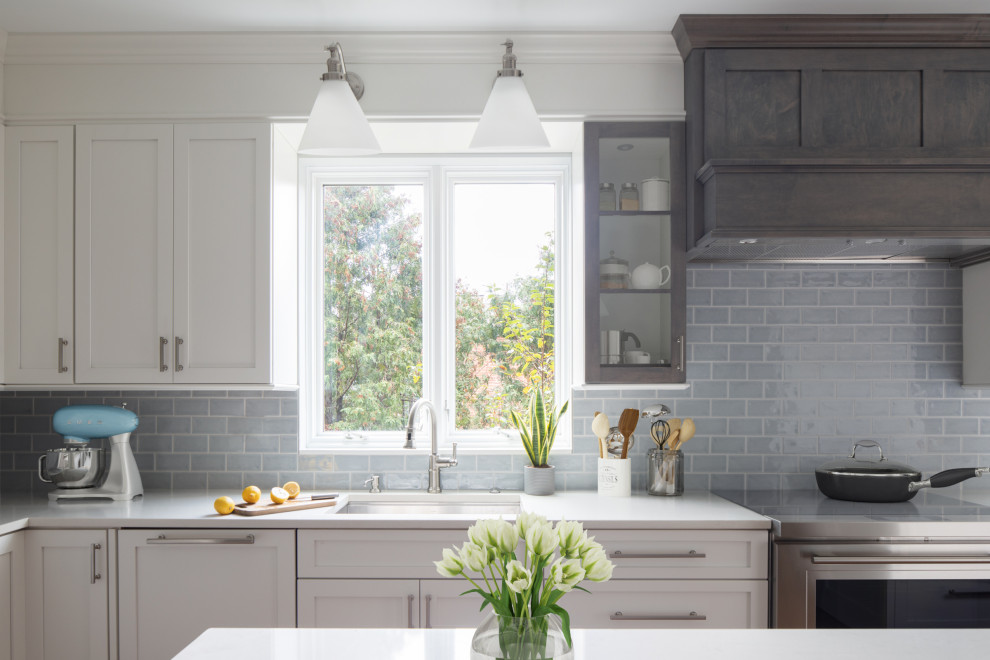 Enclosed kitchen - mid-sized transitional l-shaped medium tone wood floor and brown floor enclosed kitchen idea with an undermount sink, shaker cabinets, white cabinets, quartz countertops, blue backsplash, subway tile backsplash, stainless steel appliances, an island and white countertops
