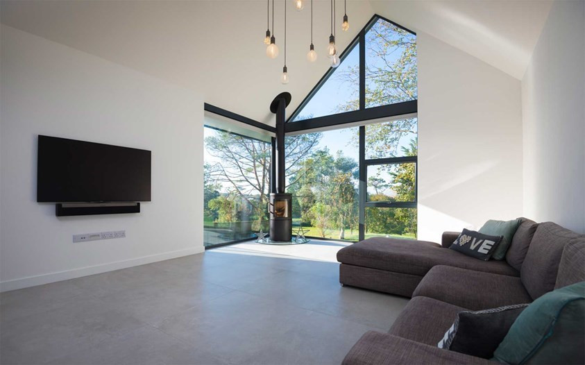 This is an example of a large contemporary living room in Cornwall with white walls, porcelain floors, a wood stove, a wall-mounted tv and vaulted.