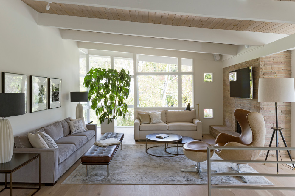 Midcentury living room in San Francisco with white walls, light hardwood floors, a standard fireplace, a stone fireplace surround and a wall-mounted tv.