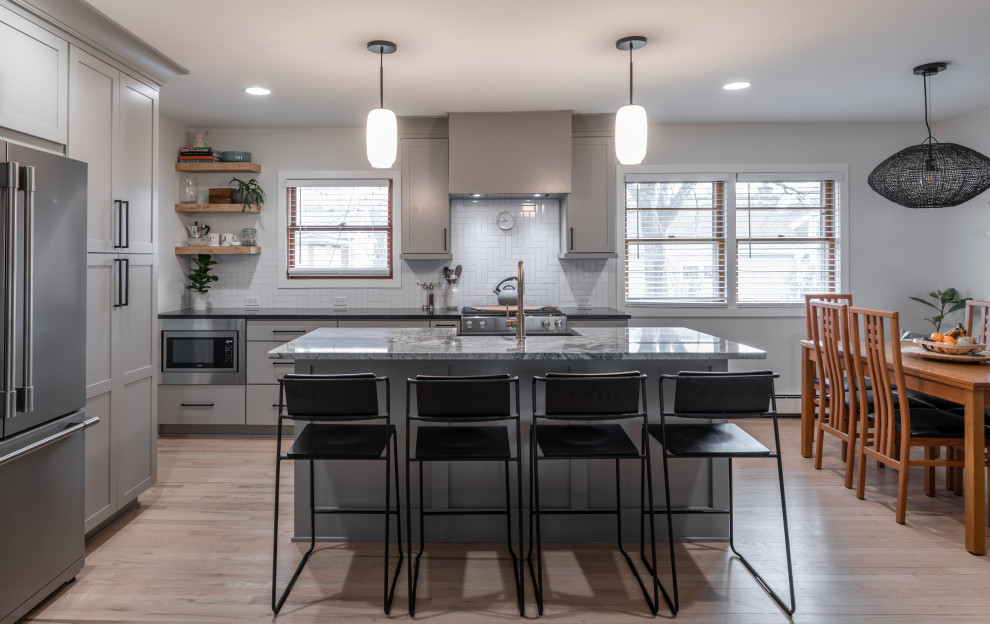 Eat-in kitchen - mid-sized modern l-shaped light wood floor eat-in kitchen idea in Chicago with a farmhouse sink, shaker cabinets, gray cabinets, granite countertops, white backsplash, ceramic backsplash, stainless steel appliances, an island and multicolored countertops