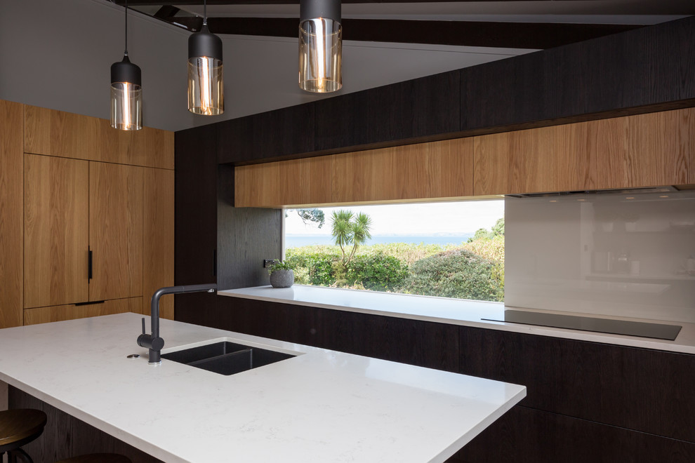 This is an example of a mid-sized contemporary l-shaped eat-in kitchen in Auckland with quartz benchtops, white splashback, glass sheet splashback, panelled appliances, medium hardwood floors, with island, an undermount sink, flat-panel cabinets, medium wood cabinets and brown floor.