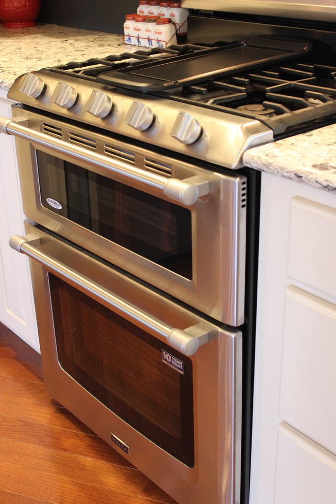 Inspiration for a large rustic l-shaped light wood floor open concept kitchen remodel in Chicago with a farmhouse sink, raised-panel cabinets, white cabinets, quartz countertops, stainless steel appliances and an island