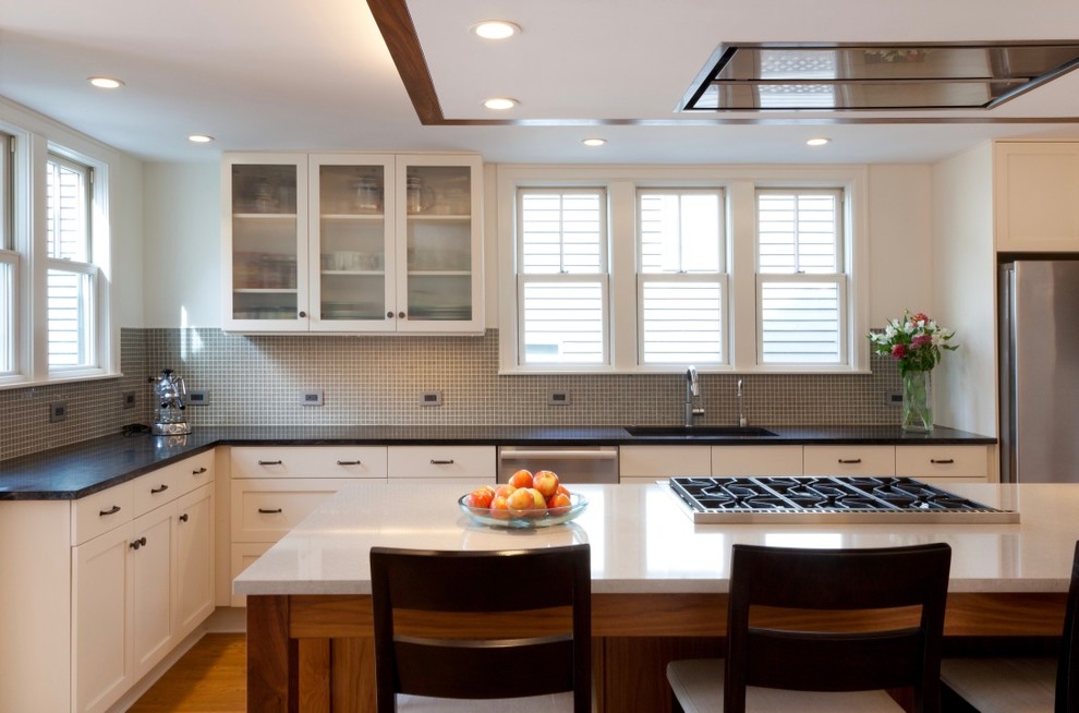 This is an example of a mid-sized transitional u-shaped eat-in kitchen in Seattle with an undermount sink, shaker cabinets, white cabinets, quartzite benchtops, grey splashback, glass tile splashback, stainless steel appliances, medium hardwood floors, with island and brown floor.