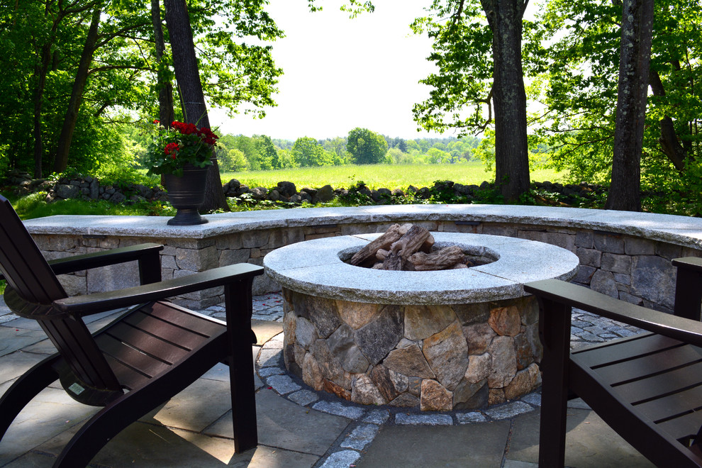 This is an example of a country backyard garden in Boston with a fire feature and natural stone pavers.