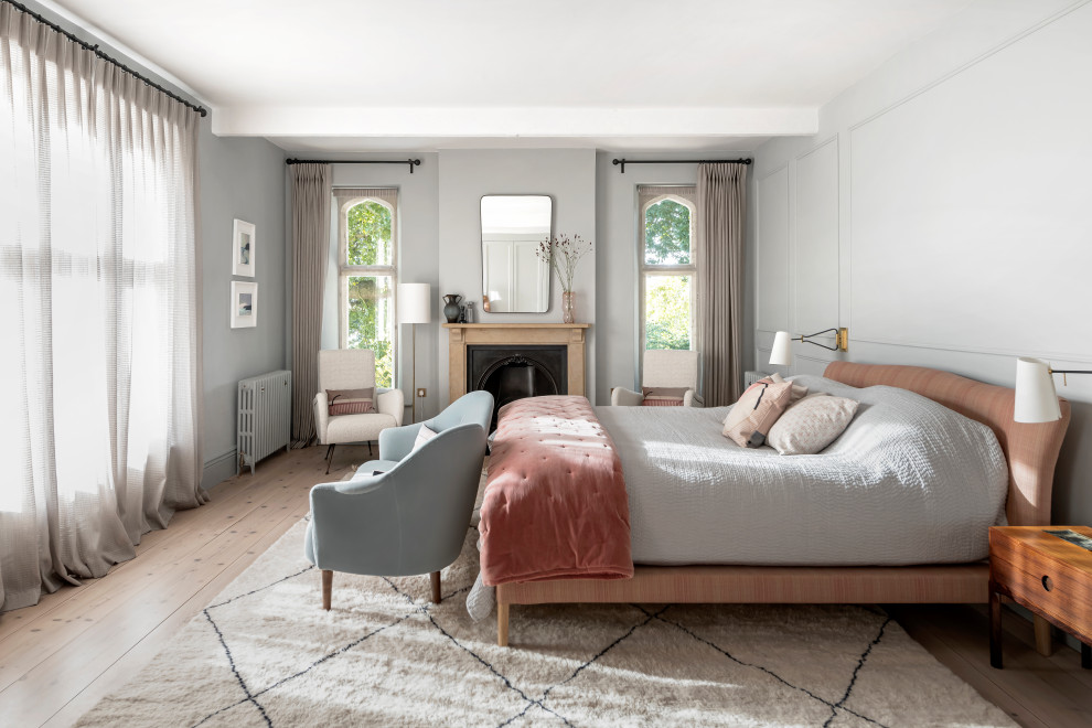 Klassisches Schlafzimmer mit grauer Wandfarbe, hellem Holzboden, Kamin, beigem Boden und Wandpaneelen in Sonstige