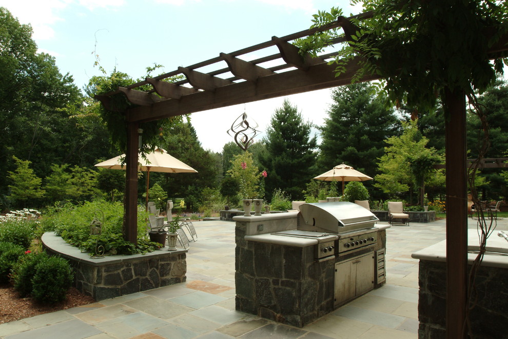 This is an example of a large traditional backyard patio in New York with an outdoor kitchen, natural stone pavers and a pergola.