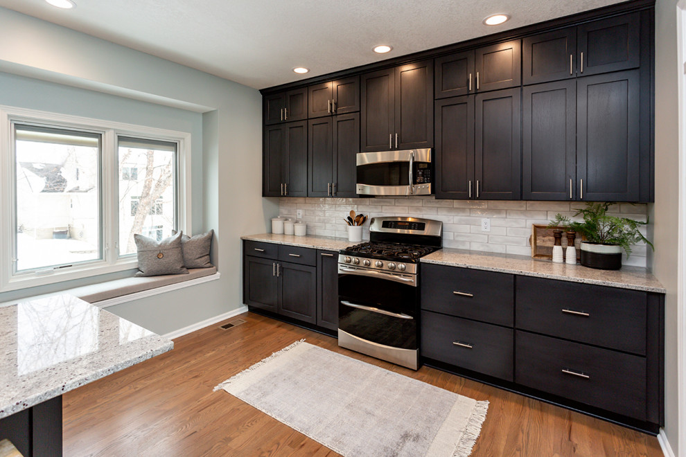 Example of a large transitional u-shaped medium tone wood floor and brown floor eat-in kitchen design with an undermount sink, recessed-panel cabinets, white cabinets, granite countertops, white backsplash, subway tile backsplash, stainless steel appliances, an island and gray countertops