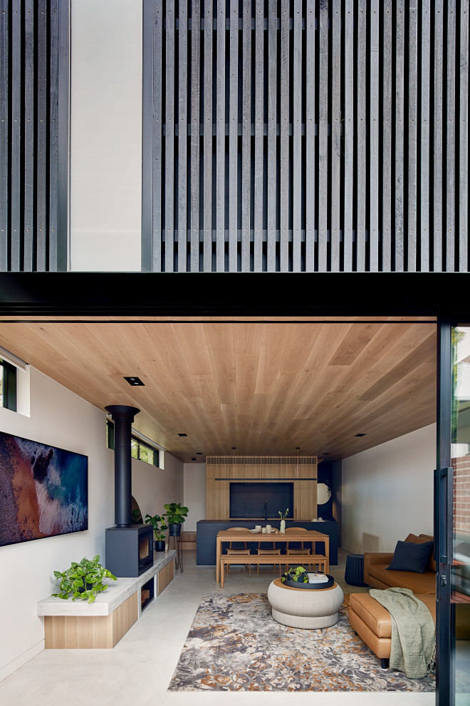 На фото: маленькая открытая гостиная комната в стиле лофт с белыми стенами, бетонным полом, печью-буржуйкой, фасадом камина из бетона, телевизором на стене, серым полом и деревянным потолком для на участке и в саду