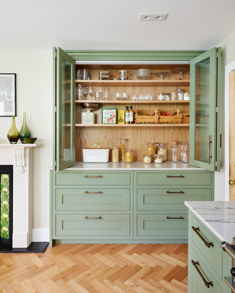 This is an example of a large traditional u-shaped eat-in kitchen in Gloucestershire with a farmhouse sink, shaker cabinets, green cabinets, quartzite benchtops, white splashback, ceramic splashback, stainless steel appliances, medium hardwood floors, no island, brown floor and multi-coloured benchtop.