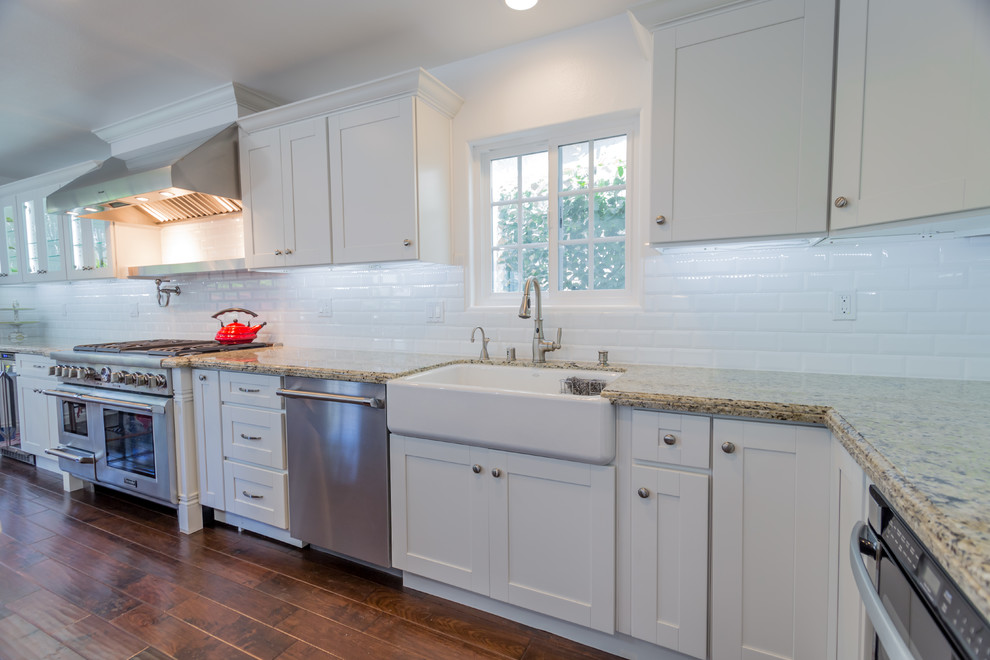 Large contemporary l-shaped eat-in kitchen in Los Angeles with a farmhouse sink, shaker cabinets, white cabinets, white splashback, subway tile splashback, stainless steel appliances, dark hardwood floors and with island.