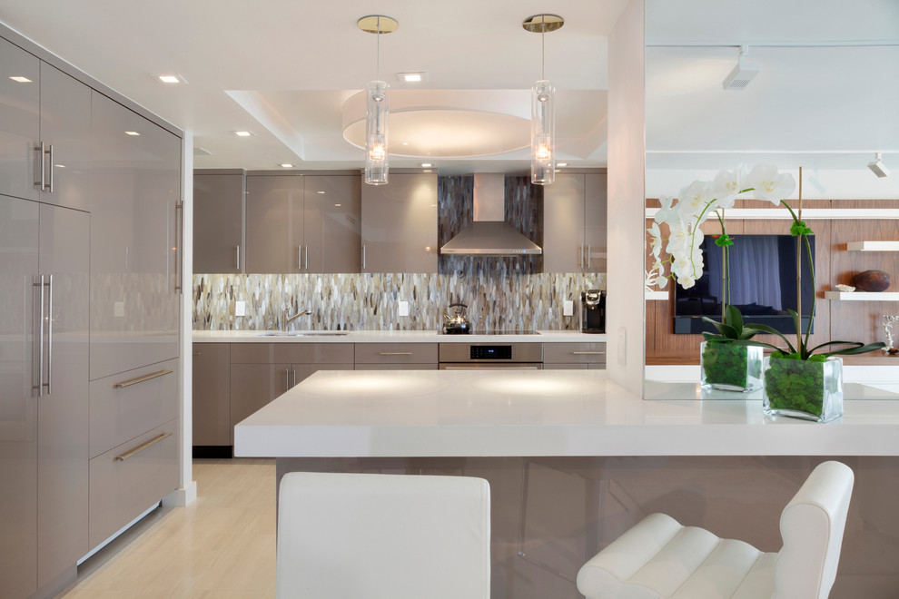 Photo of a contemporary u-shaped kitchen in Miami with a double-bowl sink, flat-panel cabinets, grey cabinets, quartz benchtops, blue splashback, glass tile splashback, stainless steel appliances, porcelain floors and with island.