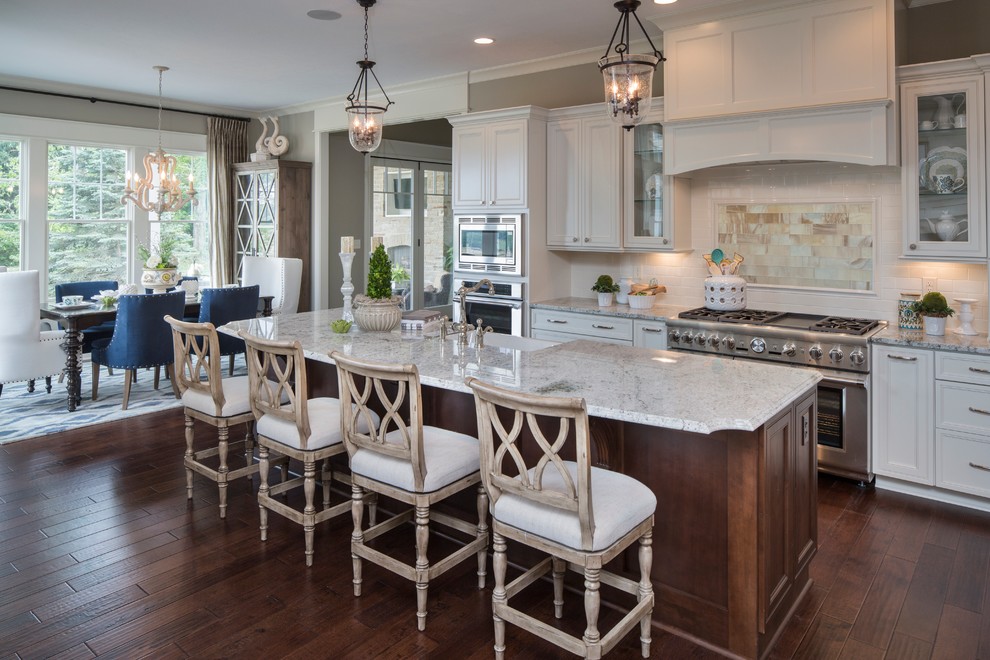 Design ideas for a traditional kitchen in Indianapolis with a farmhouse sink, recessed-panel cabinets, white cabinets, white splashback, subway tile splashback, stainless steel appliances, dark hardwood floors and with island.