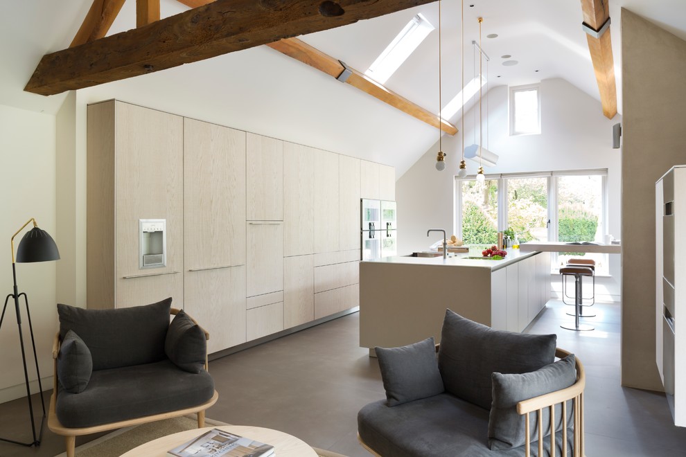 Contemporary galley open plan kitchen in Oxfordshire with a single-bowl sink, flat-panel cabinets, light wood cabinets, stainless steel appliances, concrete floors and with island.
