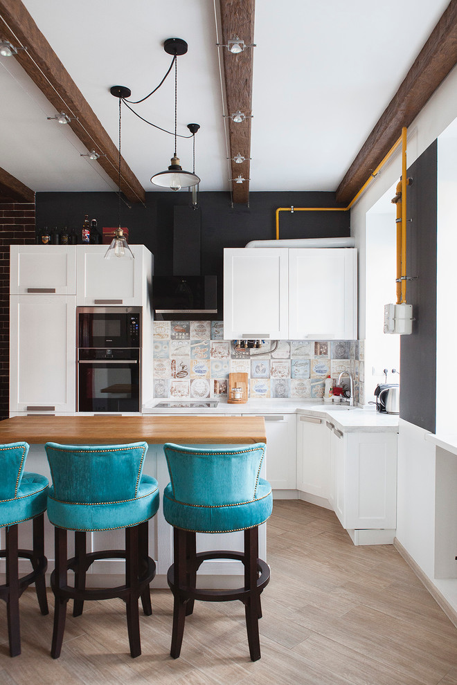 Contemporary open plan kitchen in Moscow with recessed-panel cabinets, white cabinets, multi-coloured splashback, black appliances, light hardwood floors and with island.