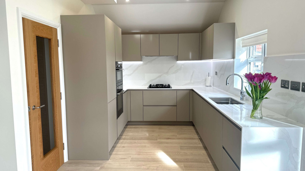 Photo of a mid-sized contemporary u-shaped separate kitchen in London with a single-bowl sink, flat-panel cabinets, grey cabinets, quartzite benchtops, white splashback, light hardwood floors, no island, brown floor and white benchtop.