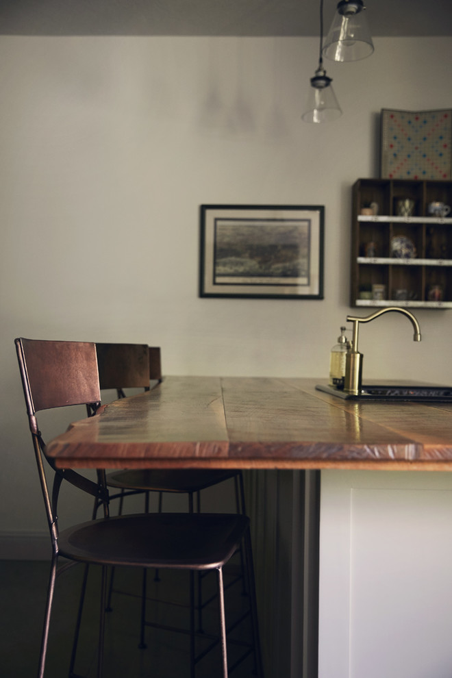 Example of a small mountain style galley concrete floor and gray floor eat-in kitchen design with a drop-in sink, shaker cabinets, white cabinets, wood countertops, white backsplash, subway tile backsplash, stainless steel appliances and brown countertops