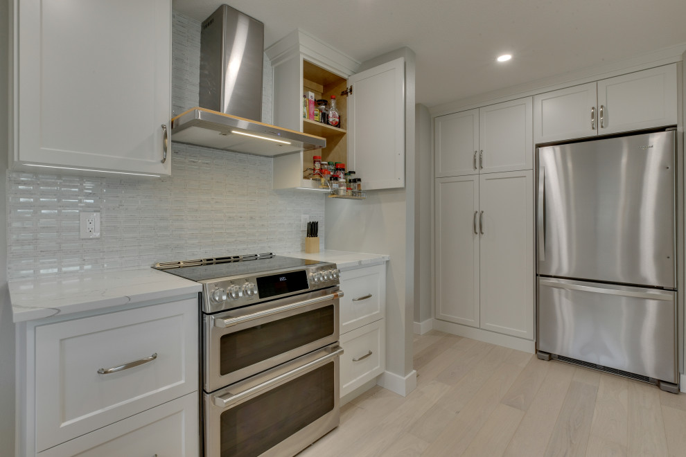 Photo of a mid-sized modern eat-in kitchen in Portland with a single-bowl sink, flat-panel cabinets, white cabinets, quartzite benchtops, white splashback, light hardwood floors, with island, beige floor and white benchtop.
