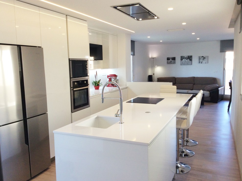 Design ideas for a mid-sized contemporary galley open plan kitchen in Alicante-Costa Blanca with an integrated sink, flat-panel cabinets, white cabinets, white splashback, stainless steel appliances, medium hardwood floors and a peninsula.