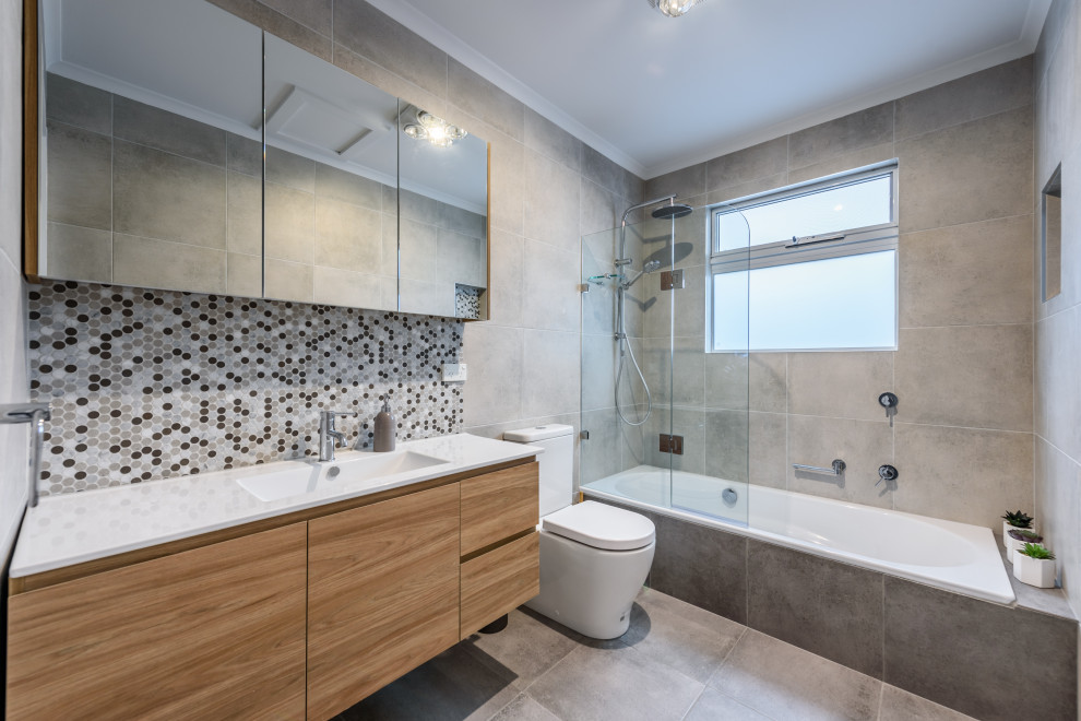 Inspiration for a mid-sized contemporary bathroom in Melbourne with a drop-in tub, a shower/bathtub combo, multi-coloured tile, grey walls, ceramic floors, marble benchtops, grey floor, white benchtops, flat-panel cabinets, medium wood cabinets, mosaic tile, an integrated sink and an open shower.