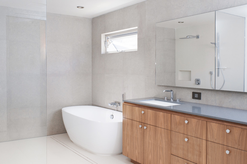 Inspiration for a large modern master bathroom in Los Angeles with flat-panel cabinets, medium wood cabinets, a freestanding tub, a curbless shower, a wall-mount toilet, white tile, ceramic tile, grey walls, ceramic floors, an undermount sink and engineered quartz benchtops.