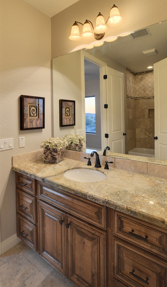 This is an example of a mediterranean bathroom in Phoenix with an undermount sink, raised-panel cabinets, medium wood cabinets, granite benchtops, an alcove tub, a shower/bathtub combo, beige tile, stone tile, beige walls and travertine floors.