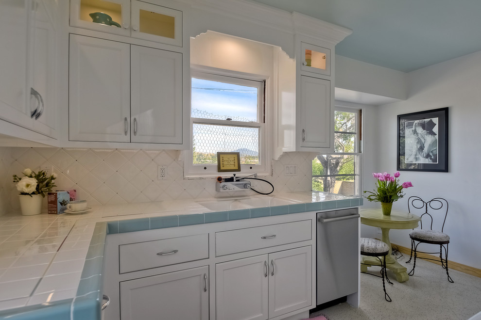 Inspiration for a mid-sized transitional galley separate kitchen in San Diego with a double-bowl sink, recessed-panel cabinets, white cabinets, tile benchtops, white splashback, ceramic splashback, white appliances, terrazzo floors and no island.