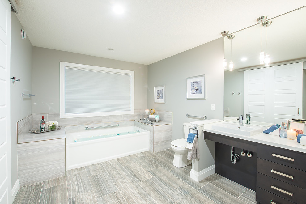 Photo of a large contemporary master bathroom in Calgary with flat-panel cabinets, dark wood cabinets, an alcove tub, a two-piece toilet, beige tile, beige walls, vinyl floors, a vessel sink, solid surface benchtops and beige floor.