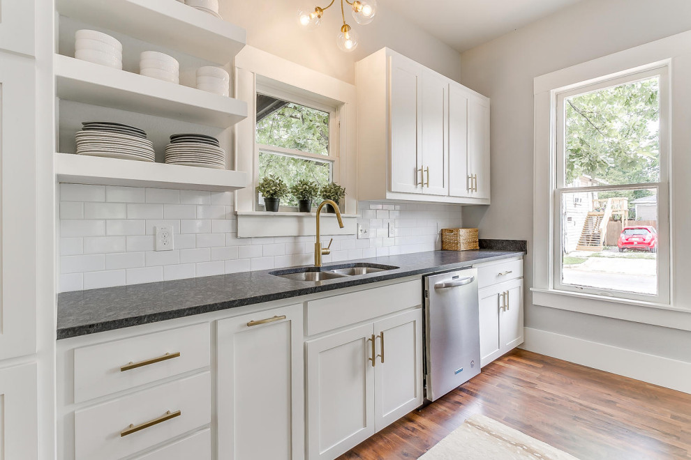 Example of a small transitional single-wall medium tone wood floor, brown floor and vaulted ceiling open concept kitchen design with a double-bowl sink, shaker cabinets, white cabinets, granite countertops, white backsplash, subway tile backsplash, an island and black countertops