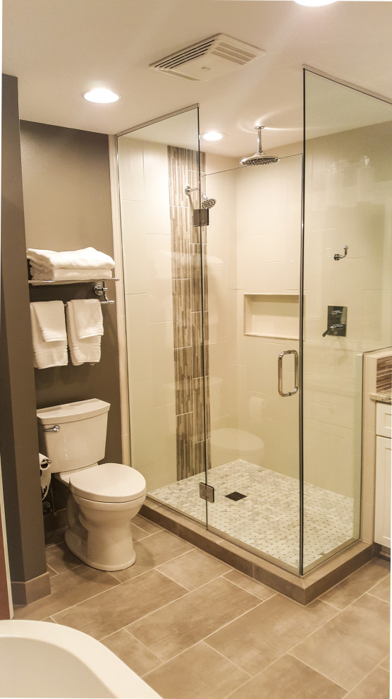 Photo of a large contemporary master bathroom in Milwaukee with shaker cabinets, white cabinets, a freestanding tub, a corner shower, a two-piece toilet, brown tile, stone tile, brown walls, porcelain floors, an undermount sink, granite benchtops, brown floor, a hinged shower door, brown benchtops, a niche, a double vanity and a built-in vanity.