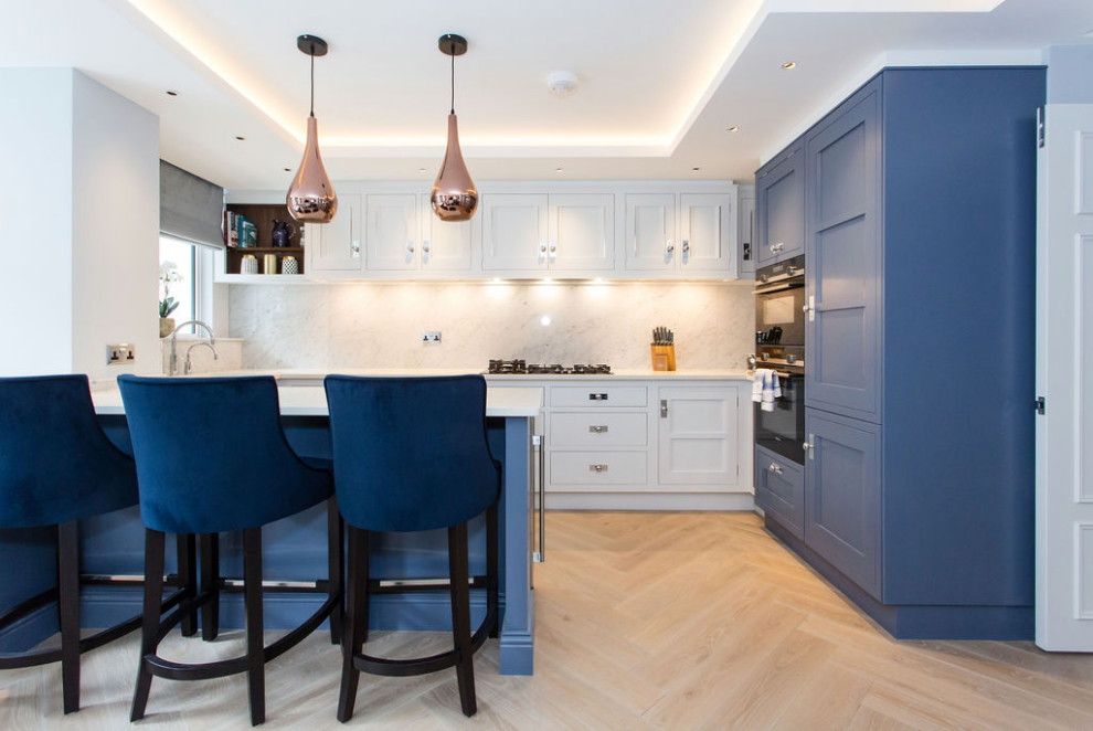 Inspiration for a small contemporary u-shaped open plan kitchen in London with a drop-in sink, recessed-panel cabinets, blue cabinets, solid surface benchtops, stone slab splashback, black appliances, light hardwood floors, a peninsula and white benchtop.
