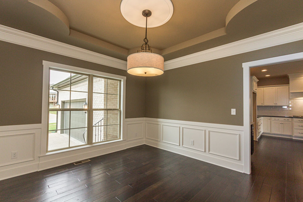 This is an example of a transitional separate dining room in Louisville with green walls, dark hardwood floors, brown floor, recessed and decorative wall panelling.