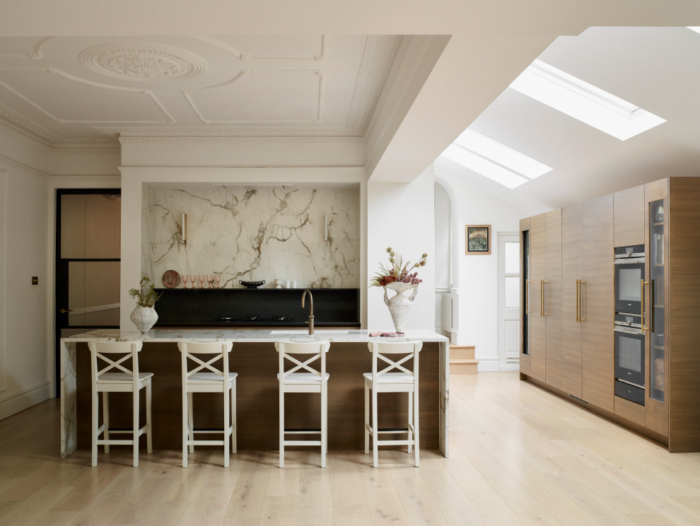 This is an example of a contemporary l-shaped kitchen in London with a submerged sink, flat-panel cabinets, medium wood cabinets, white splashback, stone slab splashback, black appliances, light hardwood flooring, an island, beige floors, white worktops and a drop ceiling.