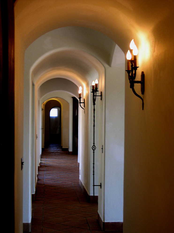 This is an example of a mid-sized mediterranean hallway in Santa Barbara with white walls, terra-cotta floors and red floor.
