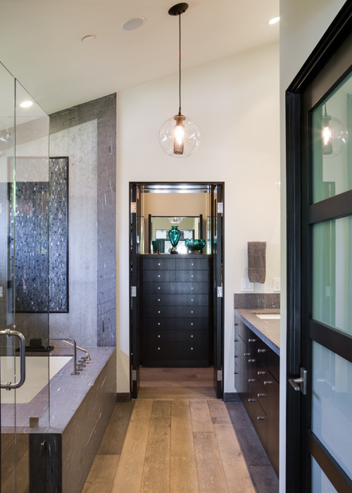 Inspiration for a large beach style master bathroom in Orange County with dark wood cabinets, an undermount tub, a shower/bathtub combo, gray tile, stone slab, white walls, light hardwood floors, a drop-in sink, limestone benchtops, brown floor and a hinged shower door.