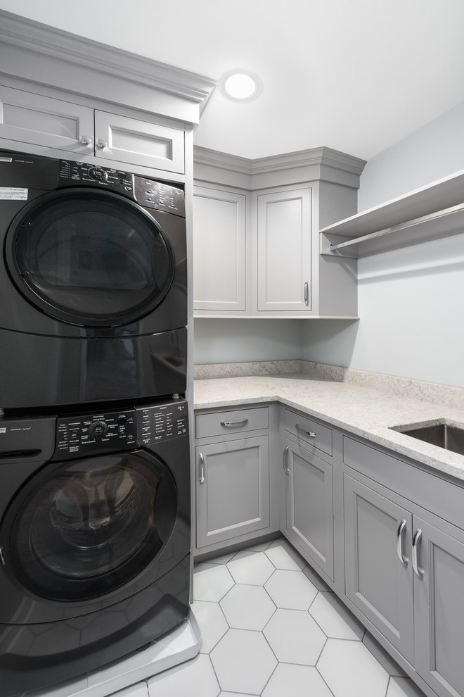 This is an example of a mid-sized transitional l-shaped dedicated laundry room in Chicago with an undermount sink, recessed-panel cabinets, grey cabinets, quartz benchtops, grey walls, carpet, a stacked washer and dryer, beige floor and white benchtop.
