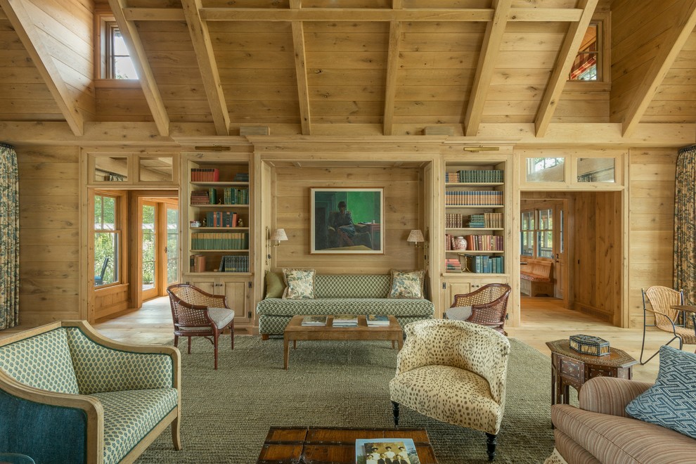 This is an example of a large country enclosed living room in New York with a library, brown walls, light hardwood floors, no fireplace, no tv and brown floor.