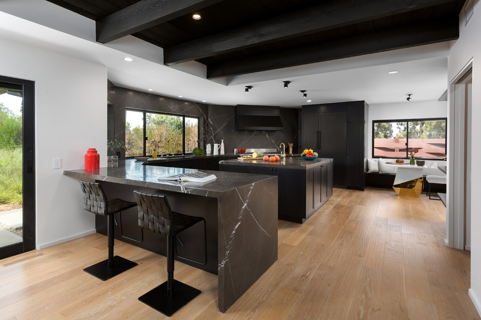 This is an example of a contemporary u-shaped open plan kitchen in Orange County with shaker cabinets, black cabinets, black splashback, panelled appliances, with island, a double-bowl sink, marble benchtops, marble splashback, light hardwood floors and beige floor.