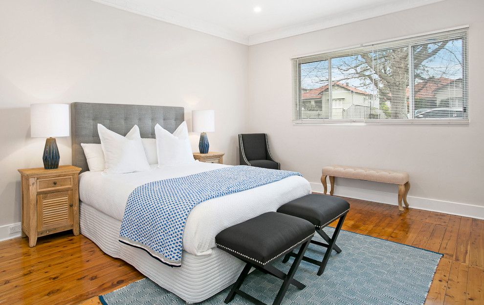 This is an example of a mid-sized transitional master bedroom in Sydney with beige walls and light hardwood floors.