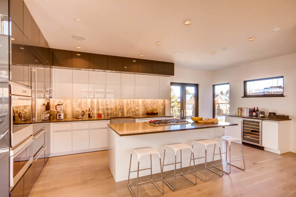 Photo of a contemporary kitchen in Denver with a farmhouse sink, flat-panel cabinets, white cabinets, brown splashback, stone slab splashback, light hardwood floors, with island, beige floor and brown benchtop.