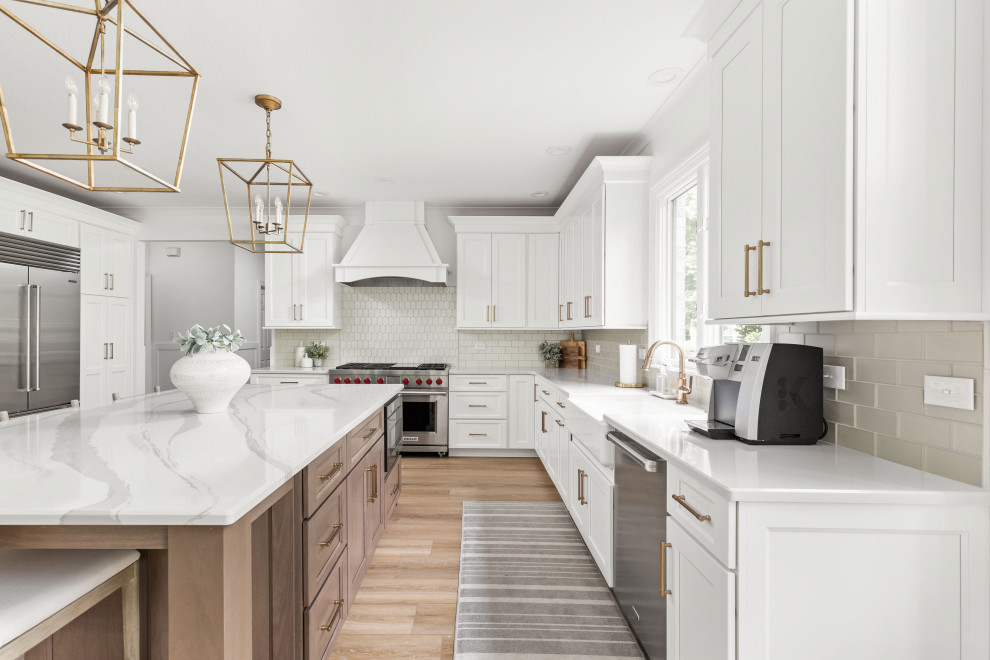 Traditional kitchen in Indianapolis with a belfast sink, shaker cabinets, white cabinets, engineered stone countertops, beige splashback, stainless steel appliances, light hardwood flooring, an island and white worktops.