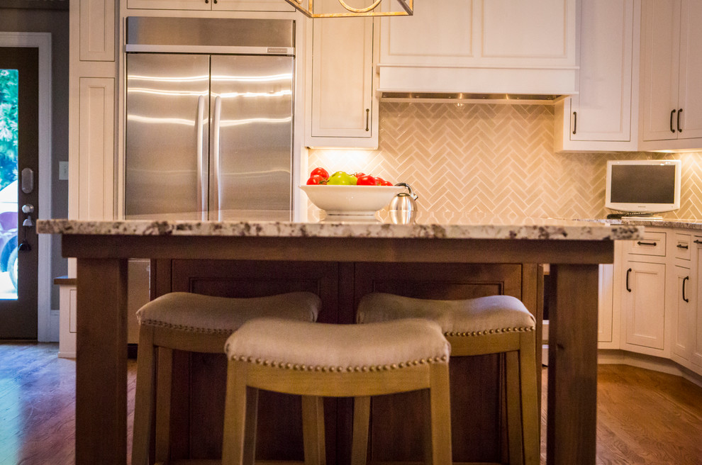 Eat-in kitchen - large transitional l-shaped medium tone wood floor eat-in kitchen idea in Atlanta with a farmhouse sink, recessed-panel cabinets, white cabinets, granite countertops, gray backsplash, glass tile backsplash, stainless steel appliances and an island