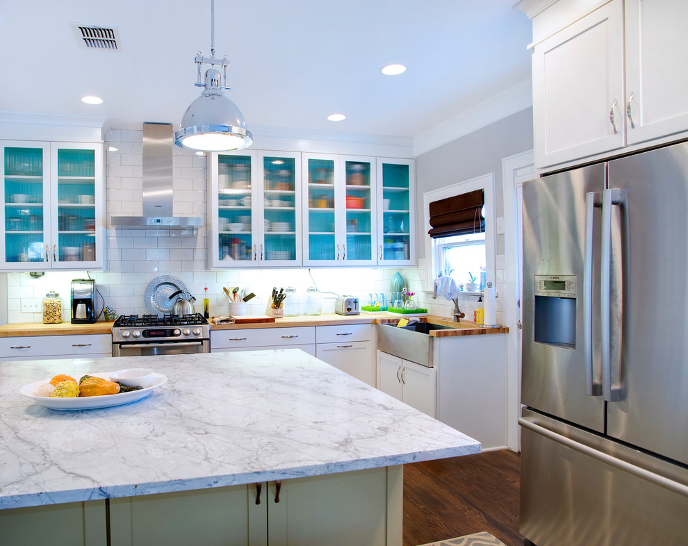 Inspiration for a contemporary kitchen in Austin with subway tile splashback, a farmhouse sink, wood benchtops, glass-front cabinets, white cabinets and stainless steel appliances.