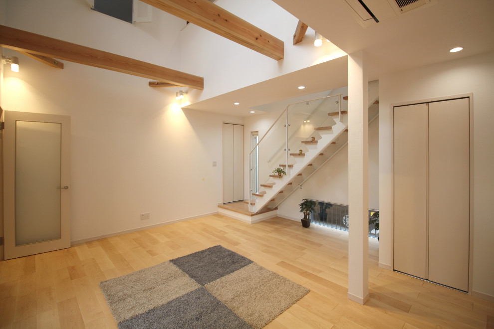 На фото: большая открытая гостиная комната в стиле модернизм с белыми стенами, деревянным полом, отдельно стоящим телевизором, бежевым полом, балками на потолке и обоями на стенах без камина