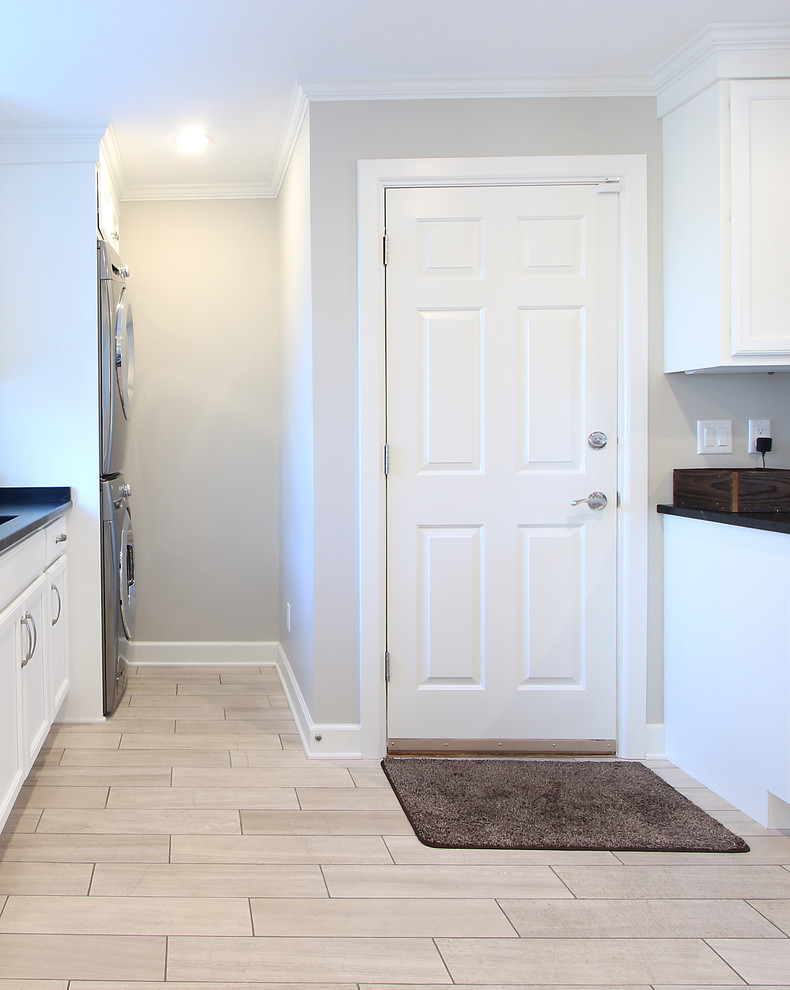 This is an example of a mid-sized transitional u-shaped utility room in Other with a single-bowl sink, flat-panel cabinets, white cabinets, soapstone benchtops, grey walls, limestone floors and a stacked washer and dryer.