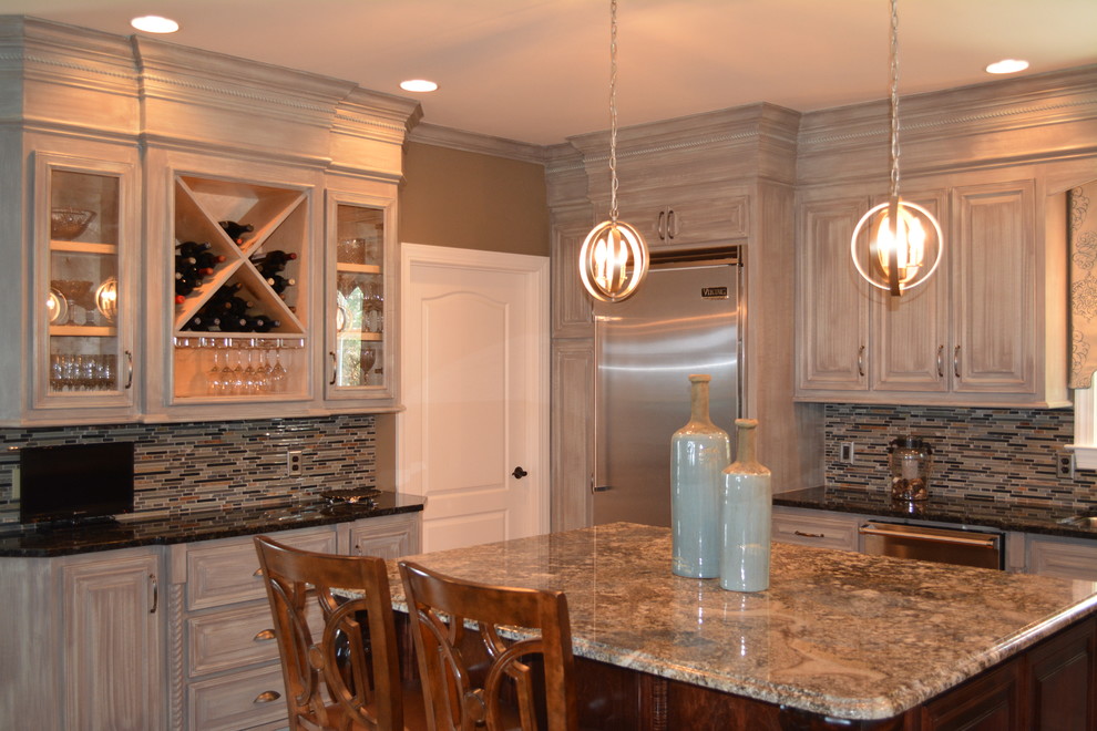 Mid-sized transitional l-shaped enclosed kitchen photo with raised-panel cabinets, distressed cabinets, granite countertops, beige backsplash, matchstick tile backsplash, stainless steel appliances and an island