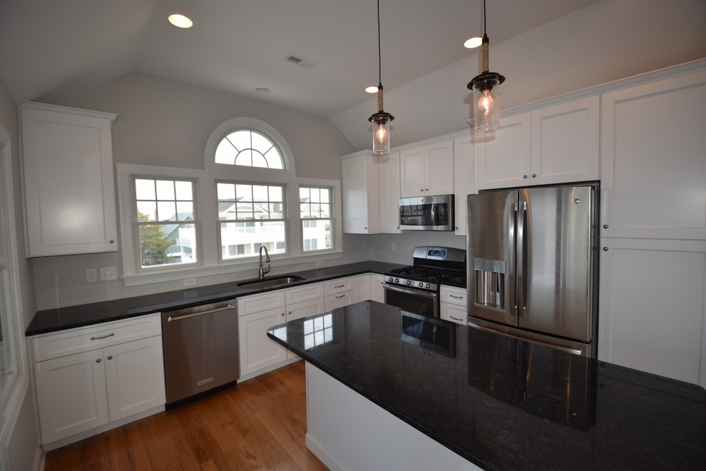 Photo of a beach style u-shaped kitchen in New York with an undermount sink, flat-panel cabinets, white cabinets, granite benchtops, stainless steel appliances, medium hardwood floors and with island.
