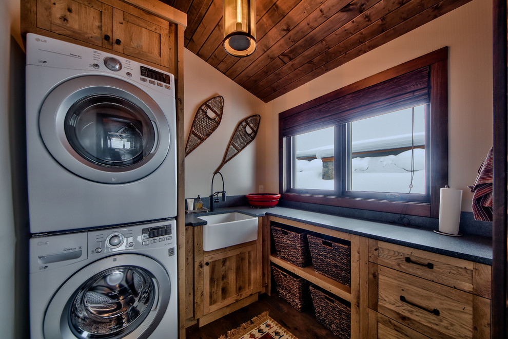 Design ideas for a mid-sized country l-shaped dedicated laundry room in Vancouver with a farmhouse sink, flat-panel cabinets, concrete benchtops, beige walls, medium hardwood floors, a stacked washer and dryer and medium wood cabinets.