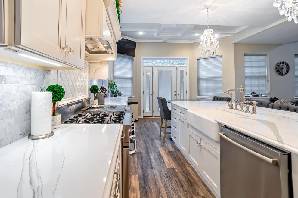 This is an example of a large transitional single-wall eat-in kitchen in Philadelphia with a farmhouse sink, shaker cabinets, white cabinets, quartz benchtops, grey splashback, porcelain splashback, stainless steel appliances, medium hardwood floors, with island, brown floor and white benchtop.